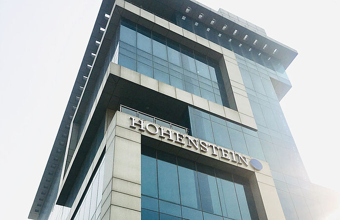 sun shining behind tall building with Hohenstein logo