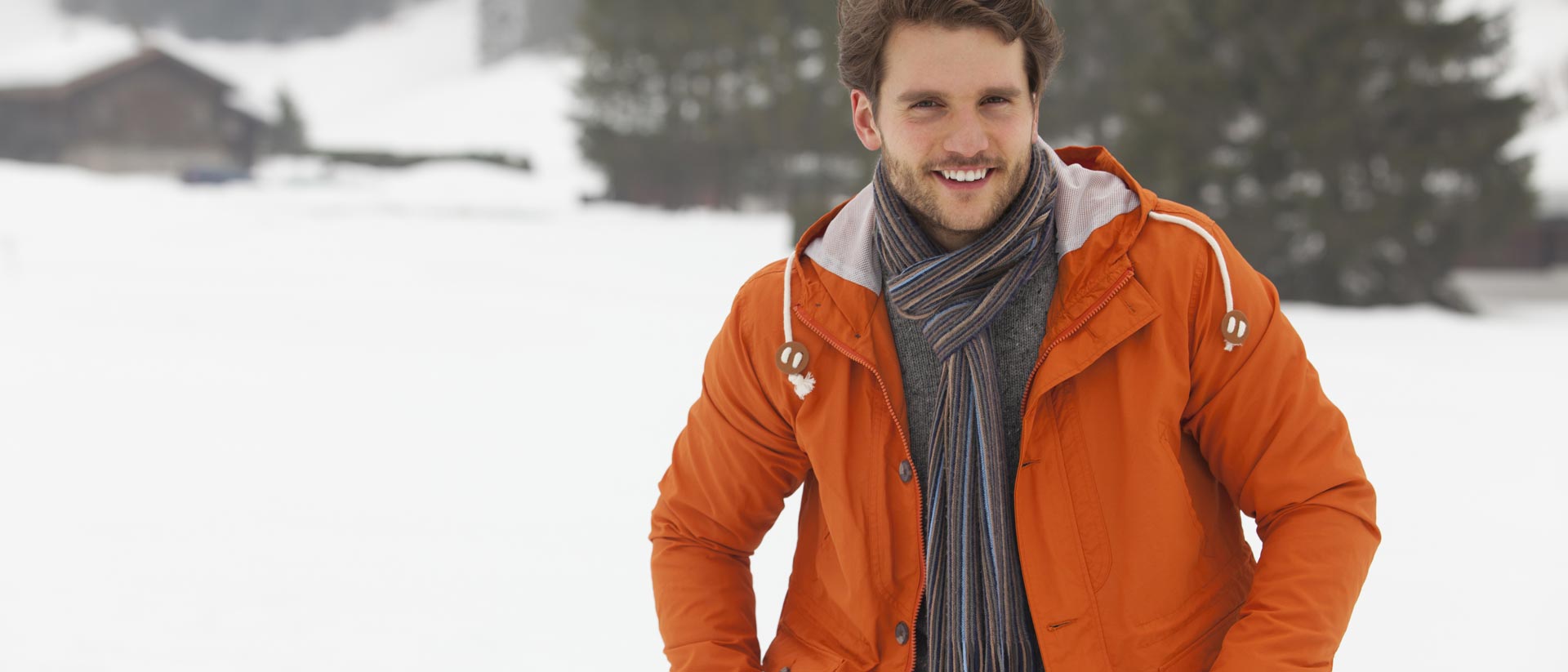 man standing in snow, wearing orange, insulated jacket and black scarf