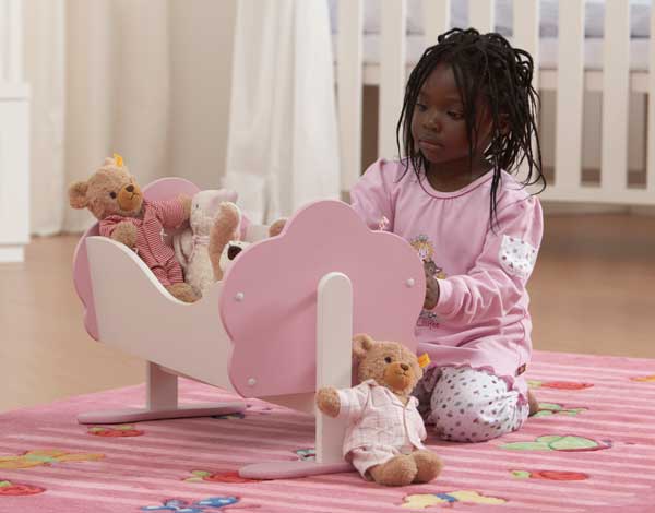 Toy Testing for Safety, Quality and Compliance. Young child wearing pink clothes, sitting on a rug with a cradle and dolls